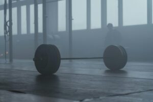 A lone barbell on the gym floor with a misty background creates a mysterious and moody ambiance.