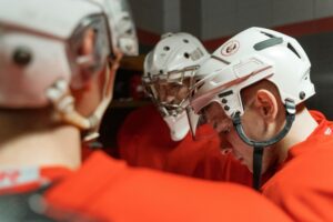 A group of male ice hockey players in helmets and uniforms huddled in a locker room preparing for a game.